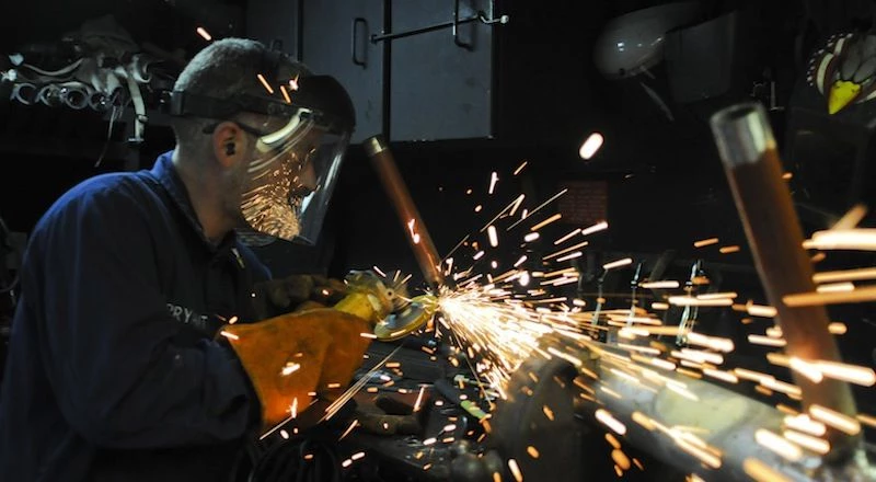 Sailor grinds a weld on a damage control training pipe patching aid aboard USS Carr