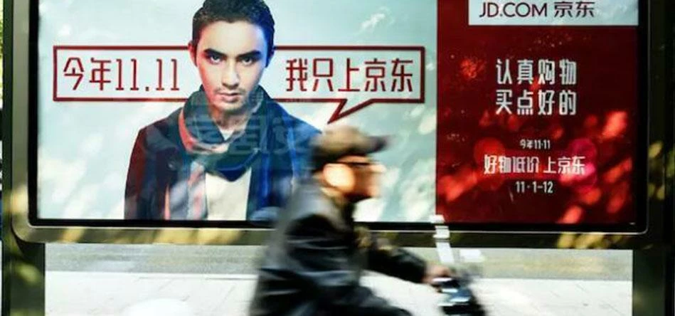 FAST LANE TO EXPORTS:  A Chinese commuter rides past one of JD.com’s Singles’ Day posters.