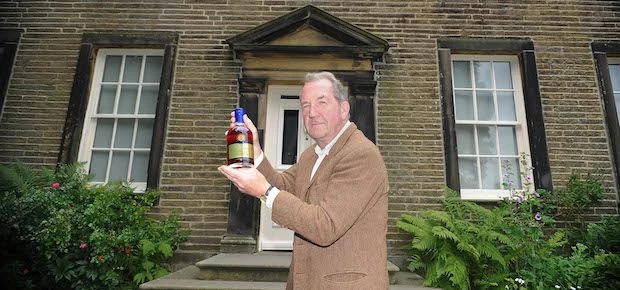 Sir James Aykroyd pictured outside Haworth Parsonage Museum with a bottle of Brontë Liqueur.