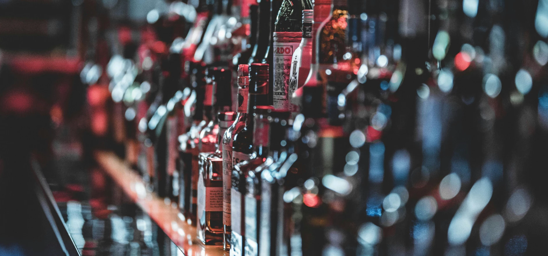 Blurred view of assorted alcohol bottles lined up on a bar shelf indoors.