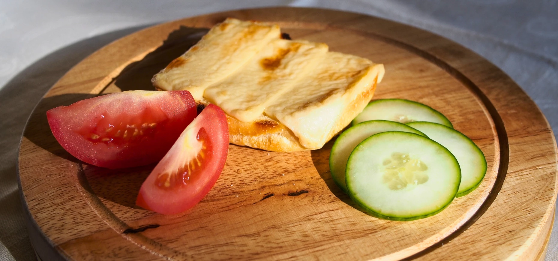 Slices of plant-based cheese sat upon a wooden board with tomatoes and cucumber.