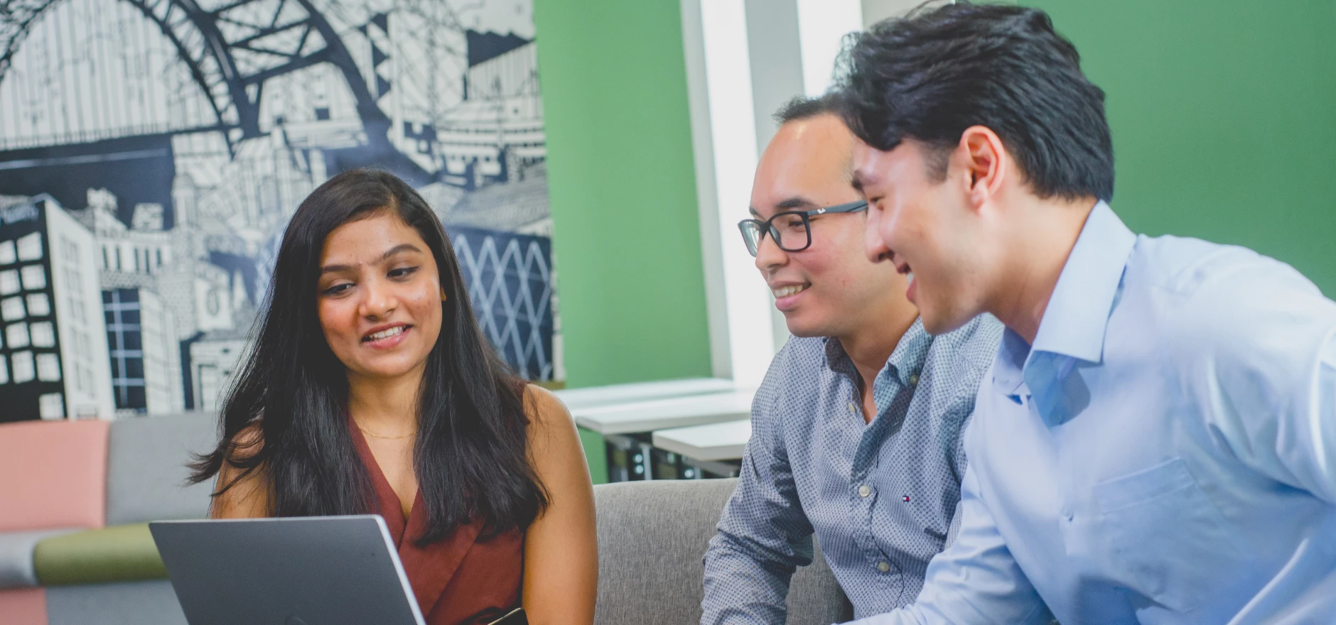 Three MBA students sat around a laptop talking and smiling