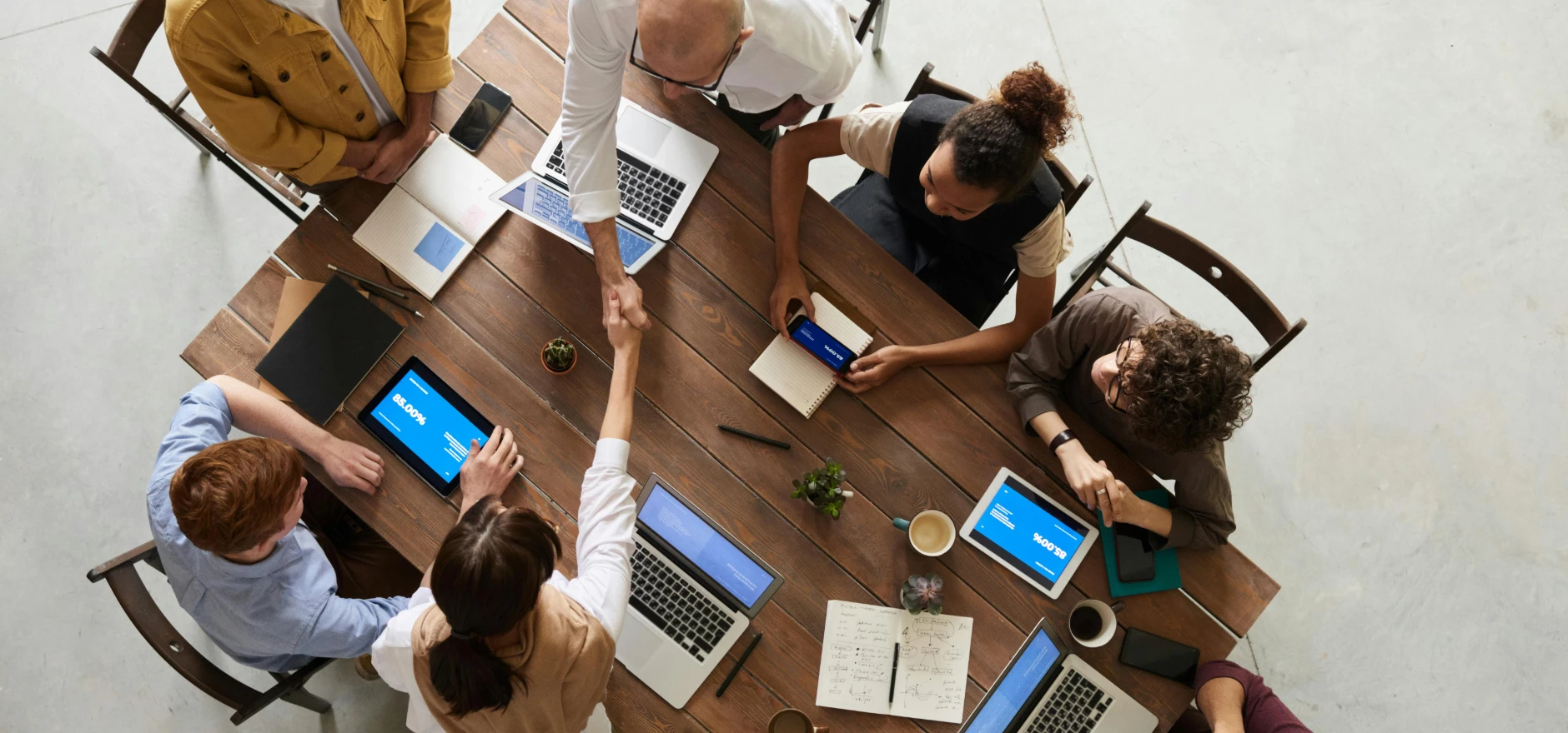 Top view of a diverse team collaborating in an office setting with laptops and tablets, promoting cooperation.