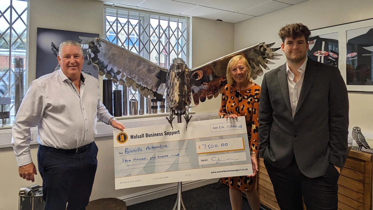 Gill Durkin from Walsall Business Support presenting a cheque to Andrew Wellings (left) and Oliver Wellings (right) in front of one of Oliver's stainless steel sculptures