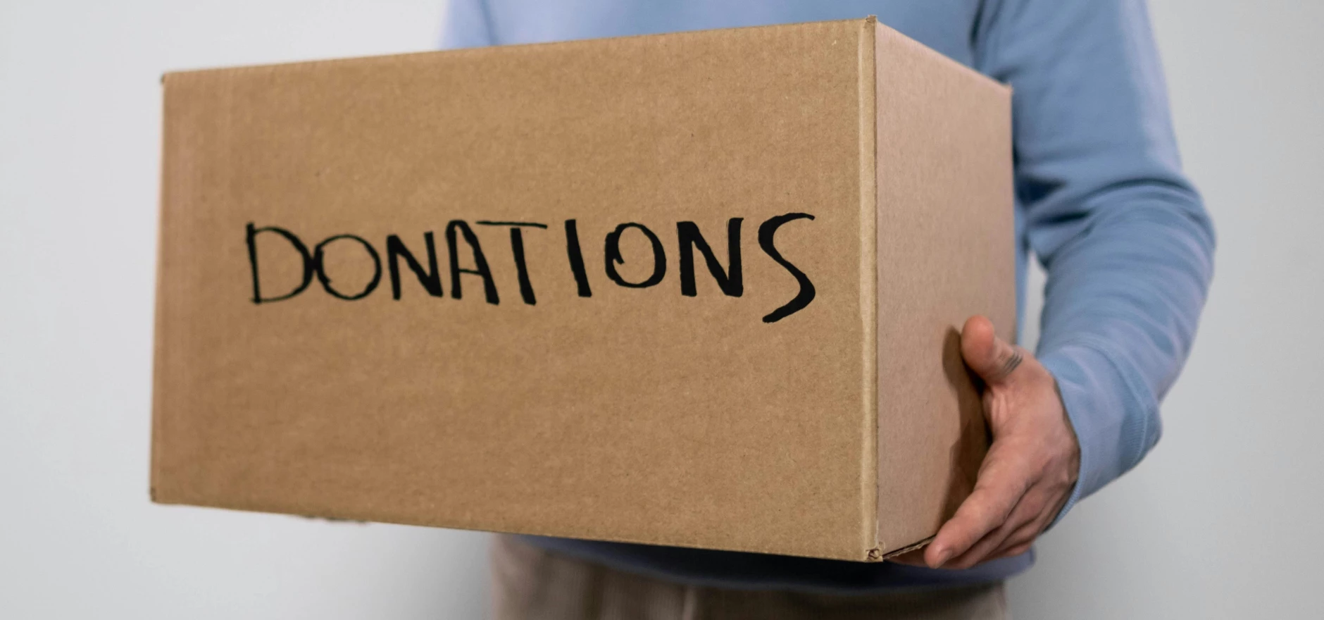 Close-up of a volunteer in a blue sweater holding a donation box. Concept of charity donations