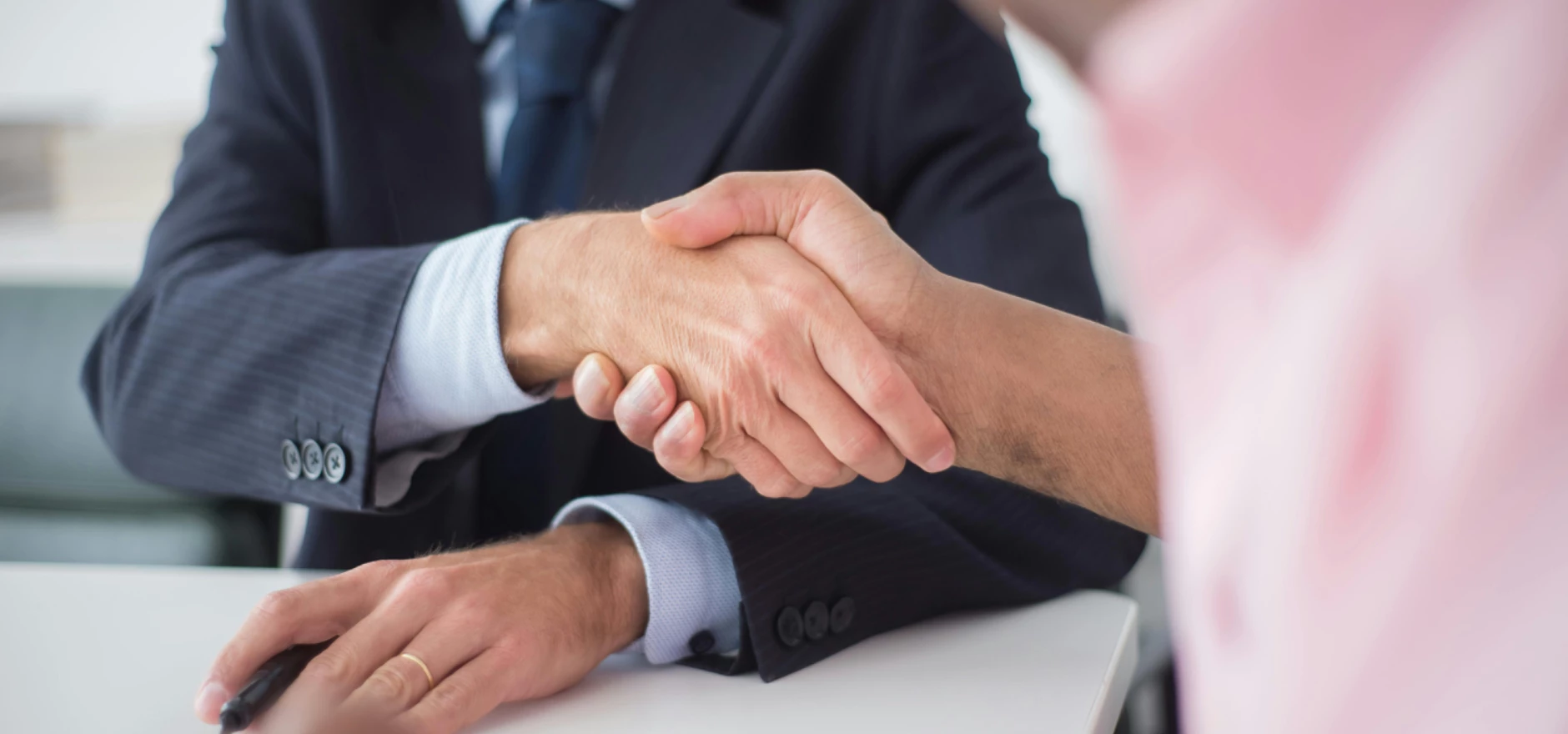 Two businessmen shaking hands across table, symbolizing agreement and partnership in an office environment.
