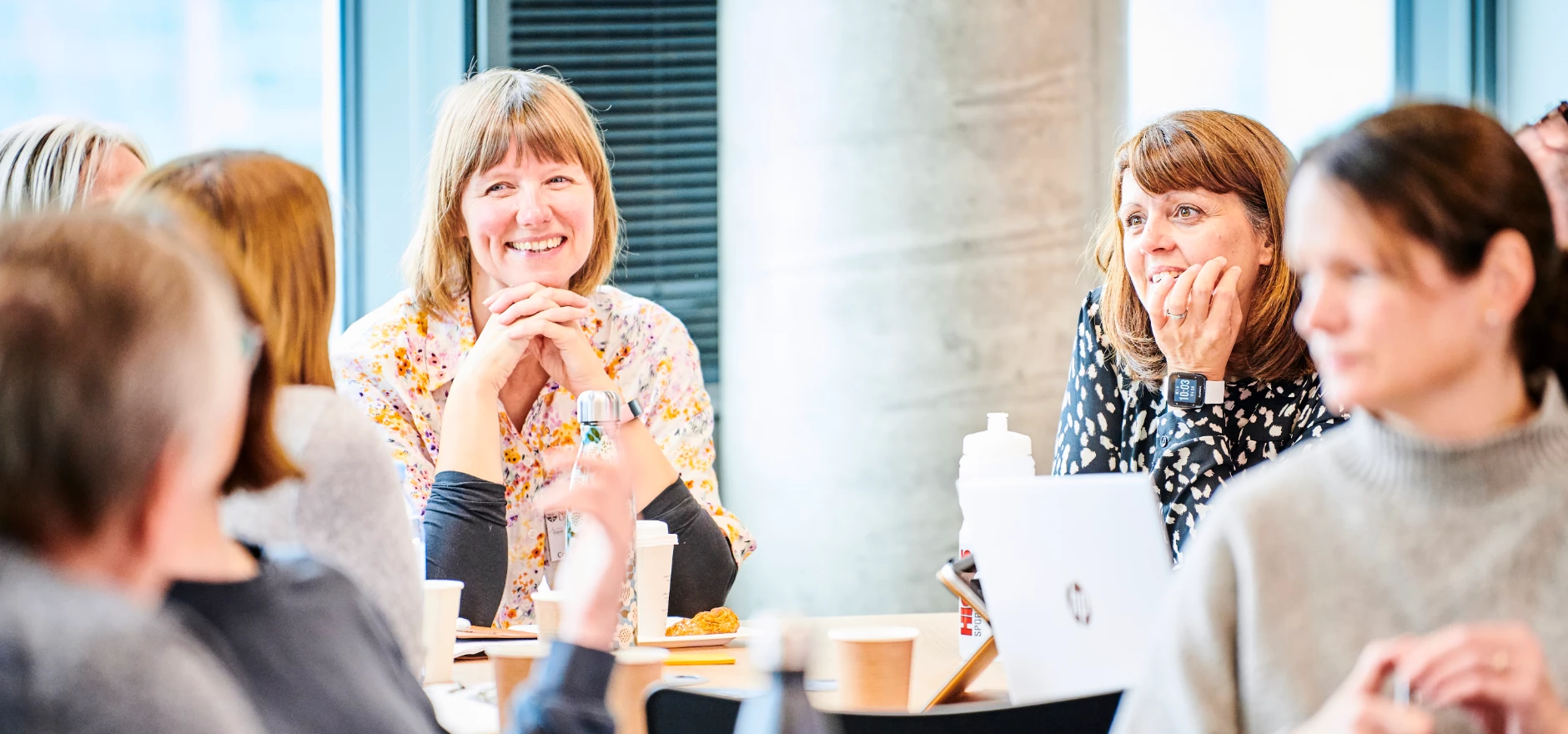 Learners sat around a table in the Business School having a conversation, smiling with laptops open and coffee cups.