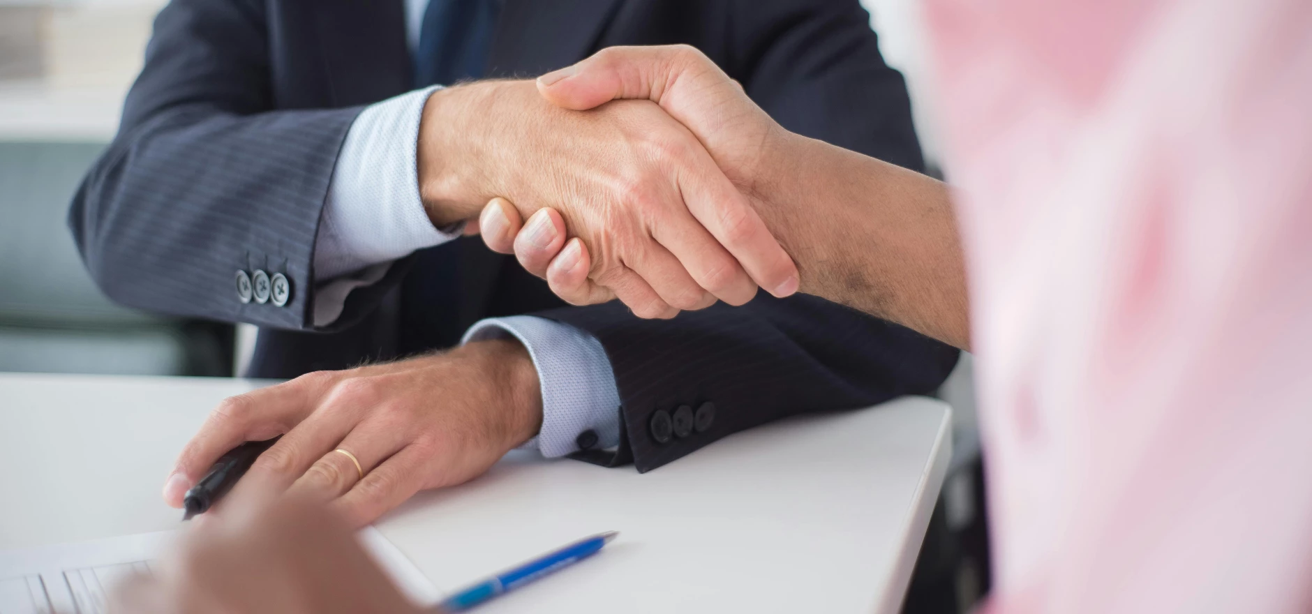 Two businessmen shaking hands across table, symbolizing agreement and partnership in an office environment.