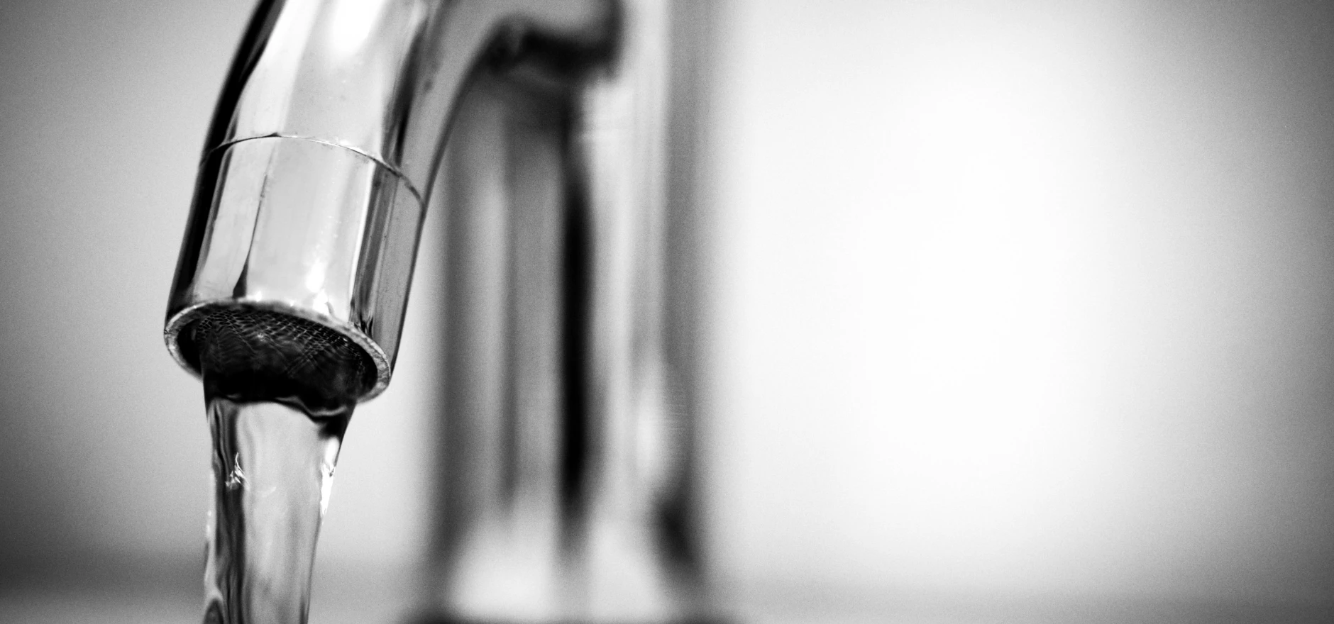 Black and white close-up of water flowing from a shiny stainless steel faucet indoors.