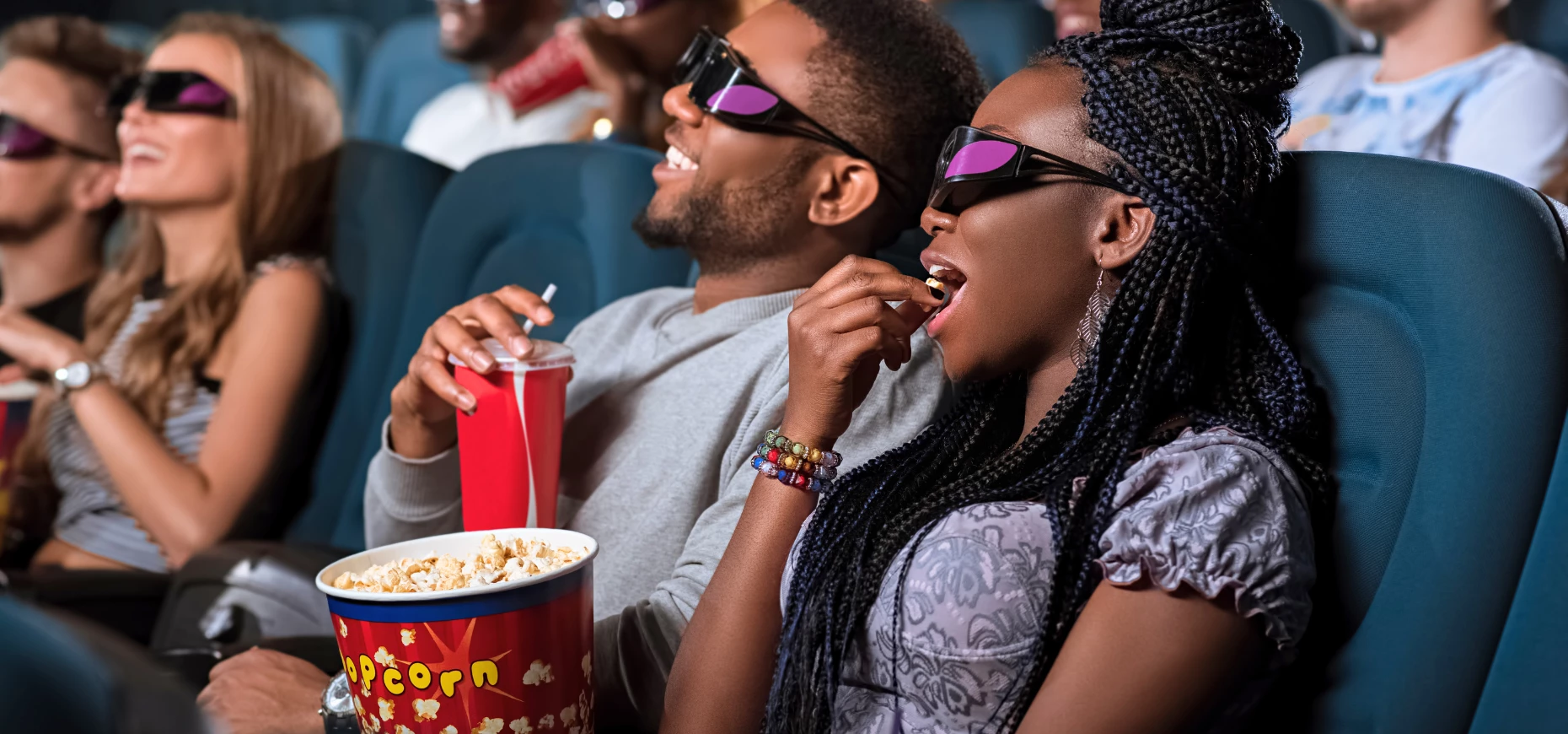 Viewers wearing 3D glasses sitting in an auditorium and eating popcorn.